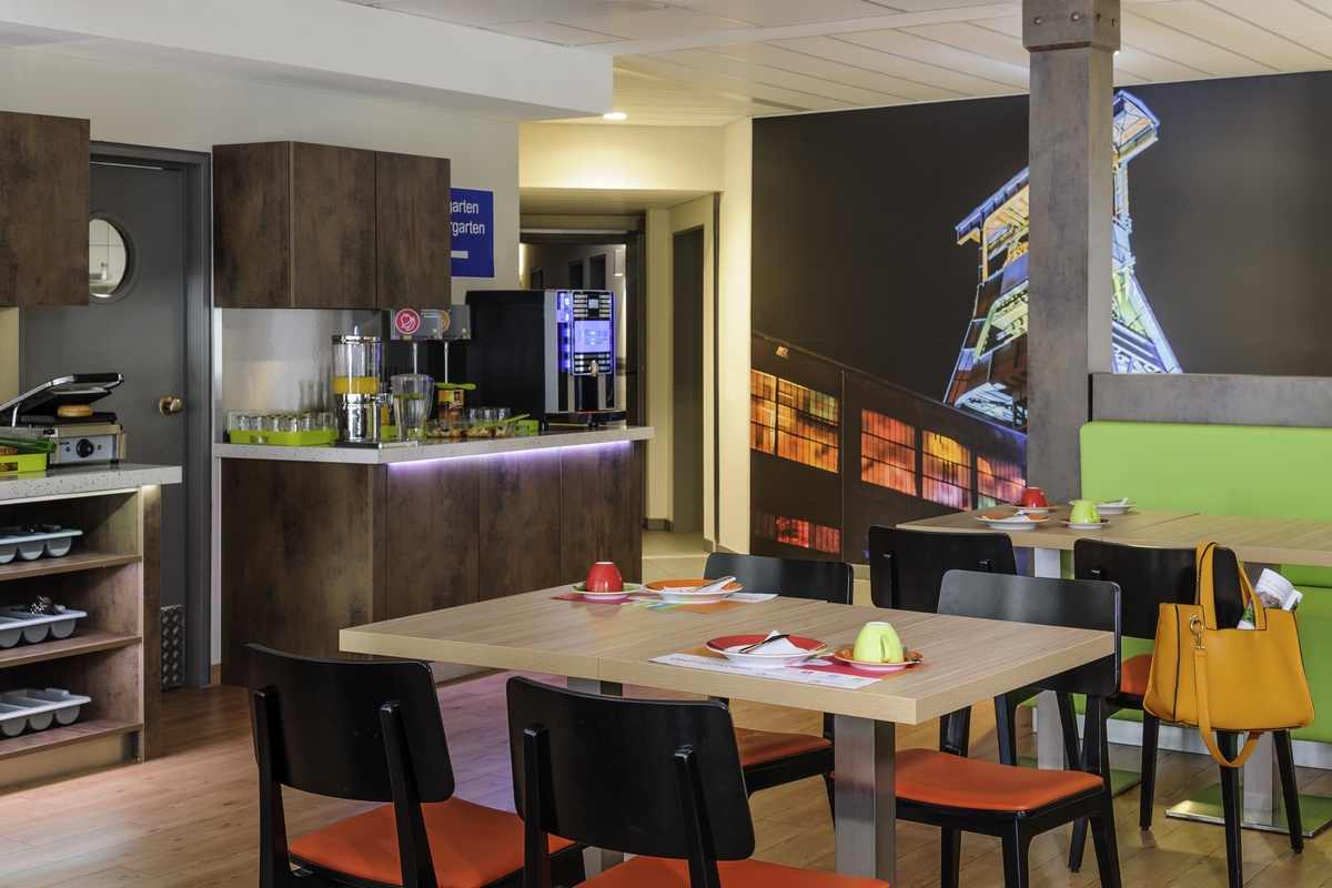 Café mit Holzmöbeln, bunten Akzenten und einem beleuchteten Foto im Hintergrund.