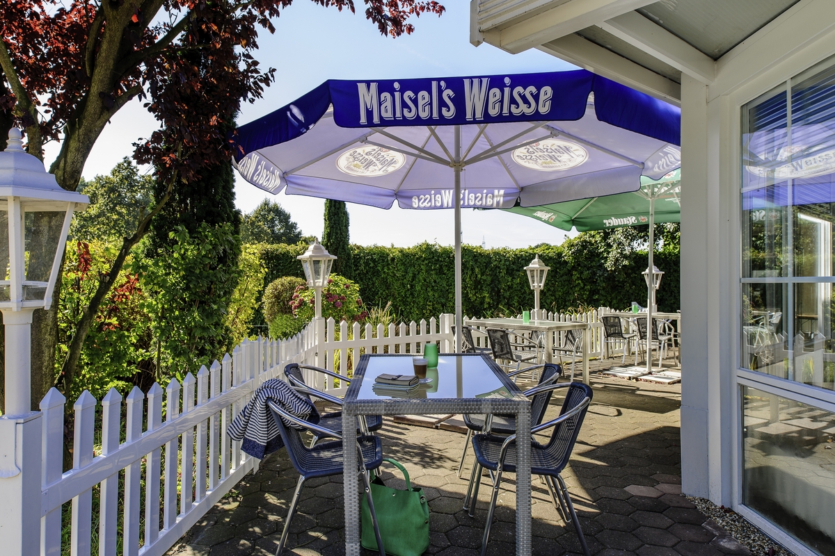Eine leere Terrasse mit blauen Stühlen, einem Sonnenschirm und Gartenblick.