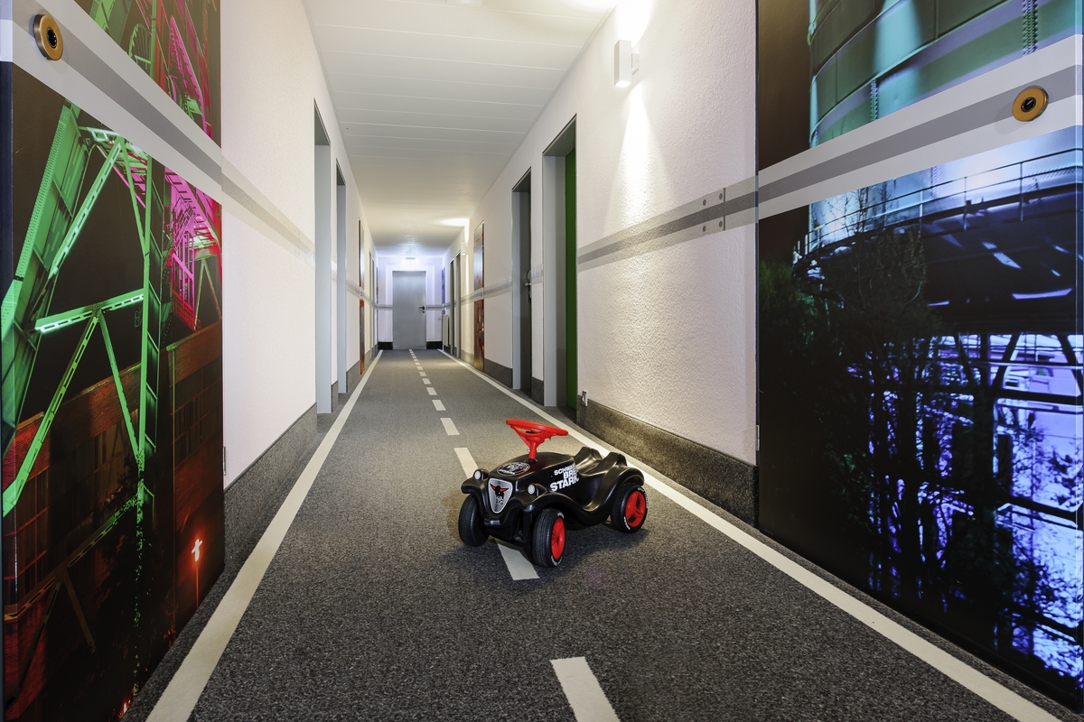 Ein Spielzeugauto steht in einem als Straße gestalteten Flur mit bunten Wandbildern.