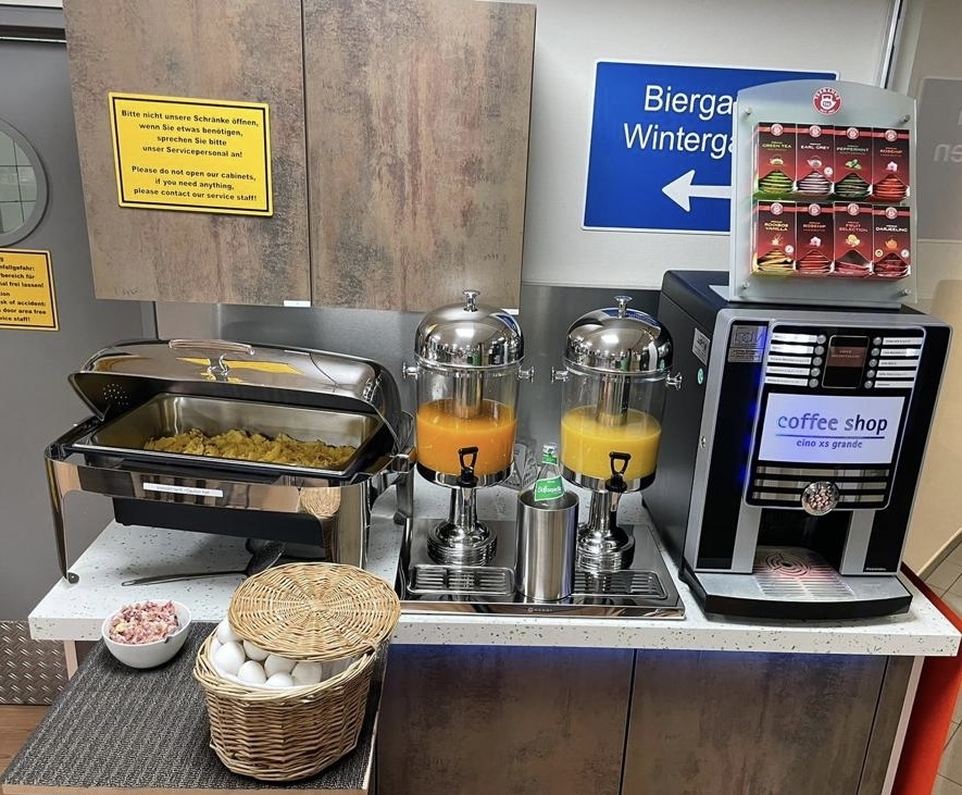 Buffet mit Rührei, Getränkespendern und Kaffeeautomat auf einem Tisch.