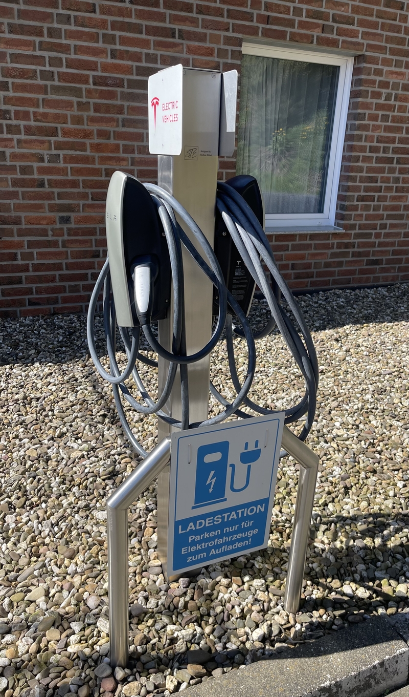 Ladestation für Elektrofahrzeuge mit zwei Steckern vor einem Backsteingebäude.