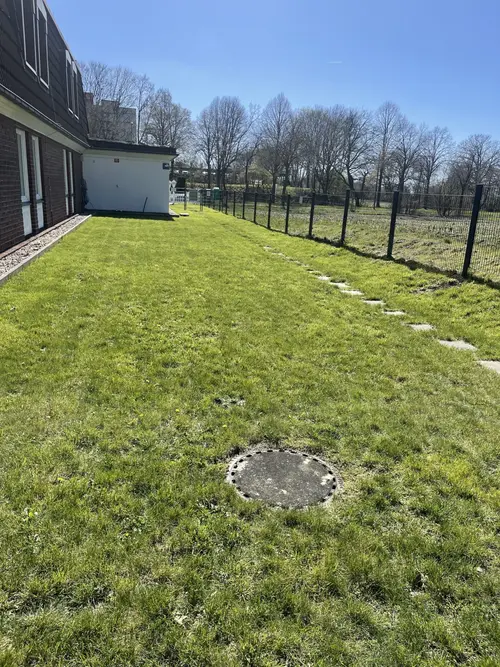 Leere grüne Wiese am Haus mit Zaun und Trittsteinen bei Sonnenschein