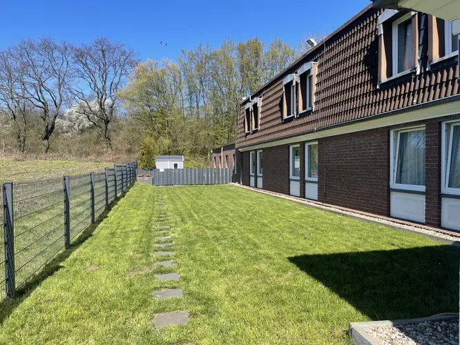 Braunes Haus mit weißen Fenstern neben grünem Rasen und Zaun bei Sonne